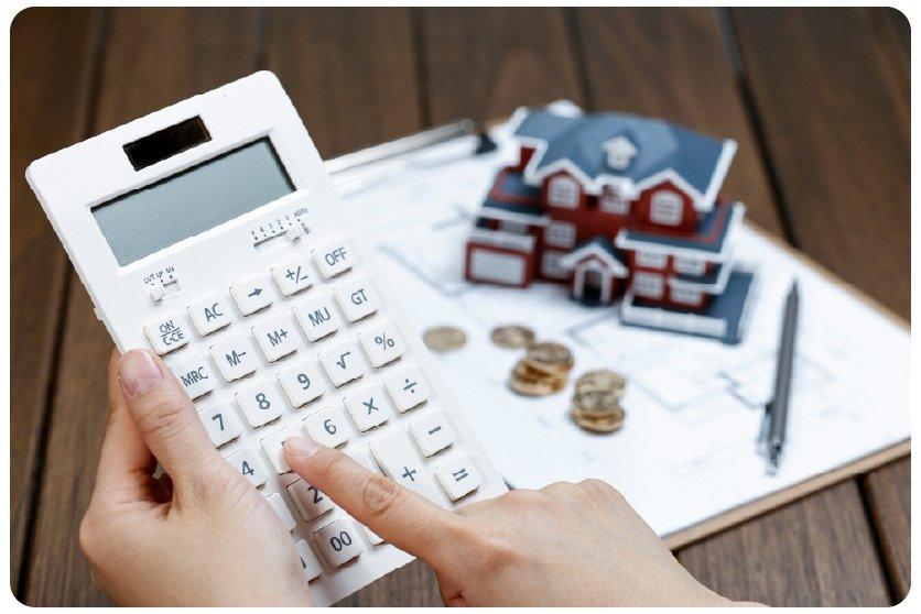 Room-by-room villa renovation budgeting — calculator, coins and a house model on architectural plans