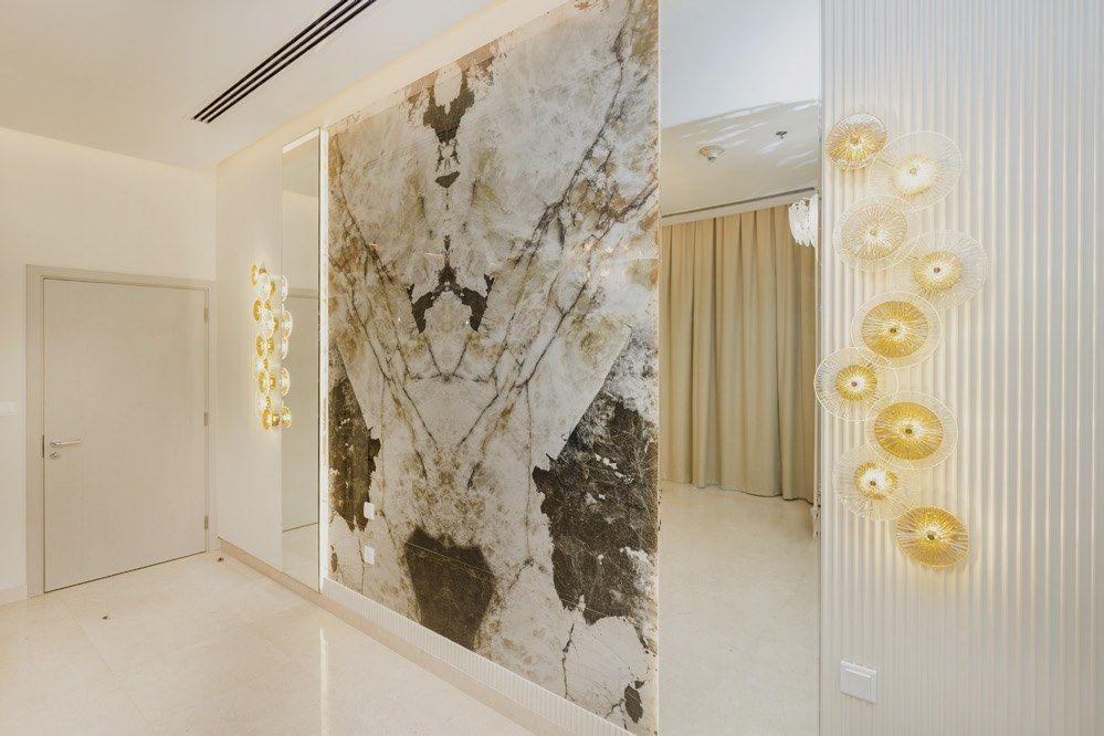 Book-matched marble feature wall and sculptural glass wall lights — penthouse interior, Dubai Creek Harbour